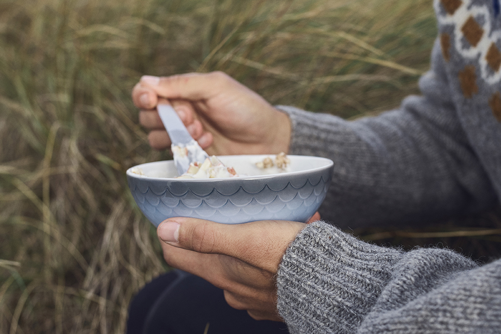 A man eating his breakfast outside from a HAV bowl while wearing a warm sweater